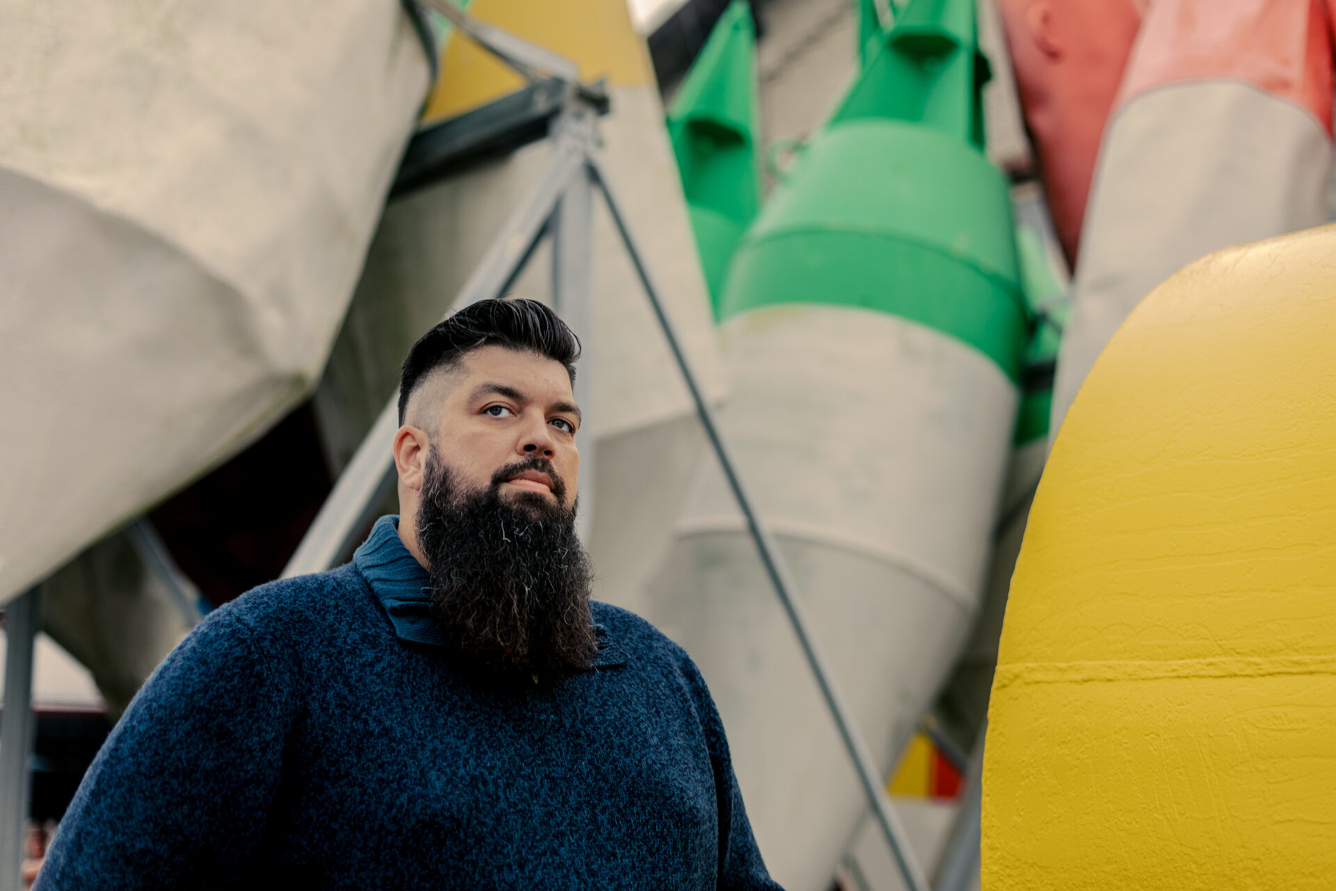 Thorsten Schwarz mit dunklem Vollbart und blauem Pullover vor gelben Seezeichen im Hafen
